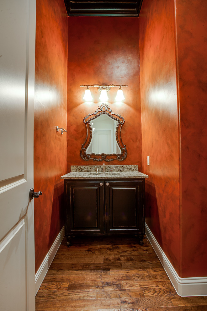 На фото: туалет в средиземноморском стиле с монолитной раковиной, темными деревянными фасадами, столешницей из гранита, унитазом-моноблоком, оранжевыми стенами и паркетным полом среднего тона с