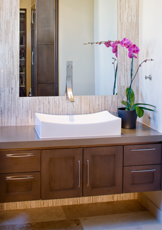 Example of a mid-sized trendy ceramic tile and multicolored floor powder room design in Austin with recessed-panel cabinets, medium tone wood cabinets, beige walls, a vessel sink and solid surface countertops