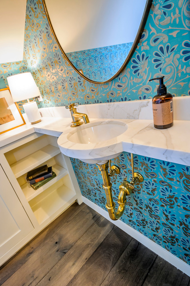 Immagine di un piccolo bagno di servizio mediterraneo con lavabo sottopiano, ante bianche, top in marmo, WC a due pezzi, pavimento in legno massello medio e pareti blu