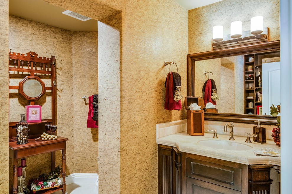 Example of a tuscan medium tone wood floor powder room design in Los Angeles with raised-panel cabinets, dark wood cabinets, a vessel sink, limestone countertops, a two-piece toilet and white walls