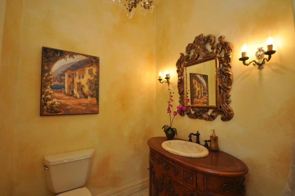 Пример оригинального дизайна: огромный туалет в средиземноморском стиле с фасадами островного типа, темными деревянными фасадами, столешницей из дерева, раздельным унитазом, бежевой плиткой, каменной плиткой, желтыми стенами, полом из травертина и накладной раковиной