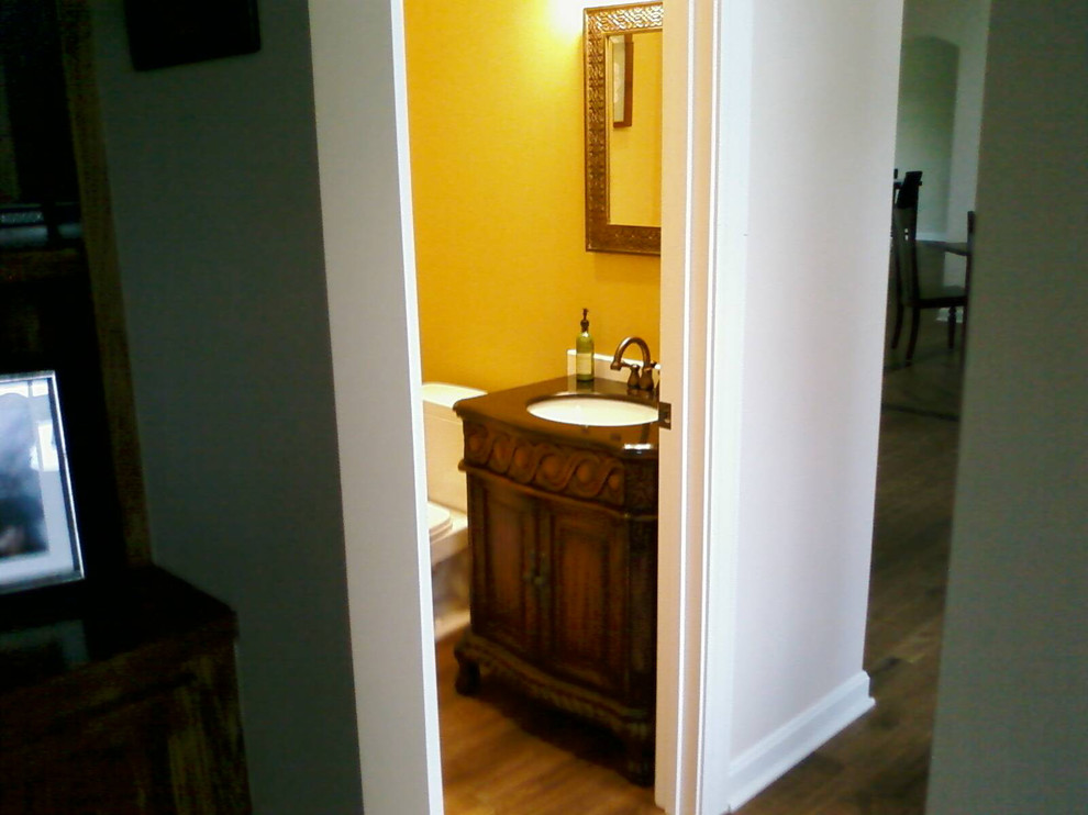 Inspiration for a small mediterranean cloakroom in Indianapolis with a submerged sink, freestanding cabinets, dark wood cabinets, granite worktops, a two-piece toilet, yellow walls and medium hardwood flooring.