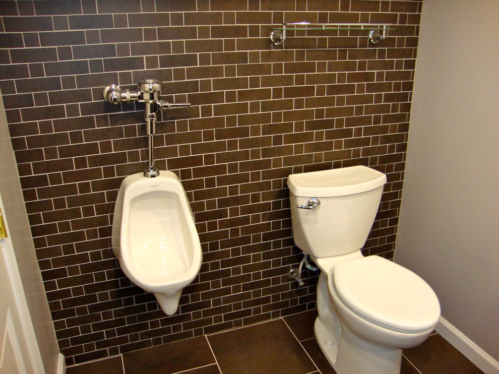 Industriell inredning av ett mellanstort toalett, med ett urinoar, luckor med infälld panel, bruna skåp, grå väggar, klinkergolv i porslin, ett undermonterad handfat, granitbänkskiva och brunt golv