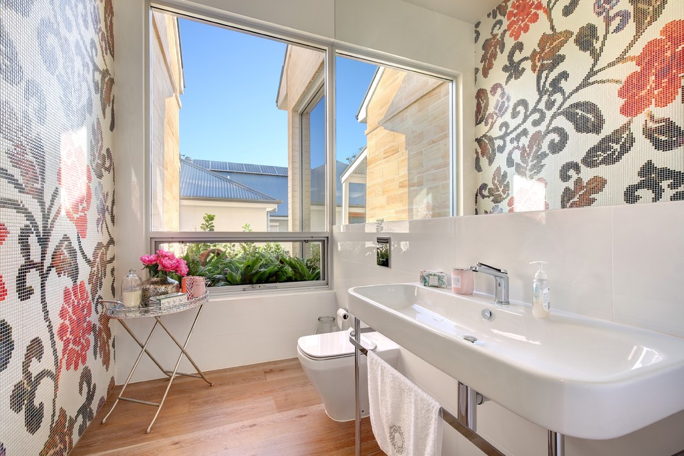 Medium sized contemporary cloakroom in Adelaide with a one-piece toilet, pink tiles, white tiles, mosaic tiles, multi-coloured walls, medium hardwood flooring, brown floors and a wall-mounted sink.