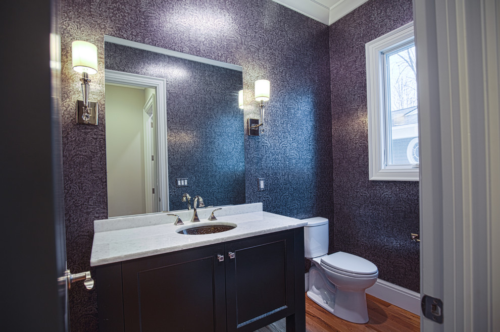 Inredning av ett klassiskt stort toalett, med luckor med profilerade fronter, mellanmörkt trägolv, ett undermonterad handfat, en toalettstol med separat cisternkåpa, lila väggar, marmorbänkskiva och svarta skåp