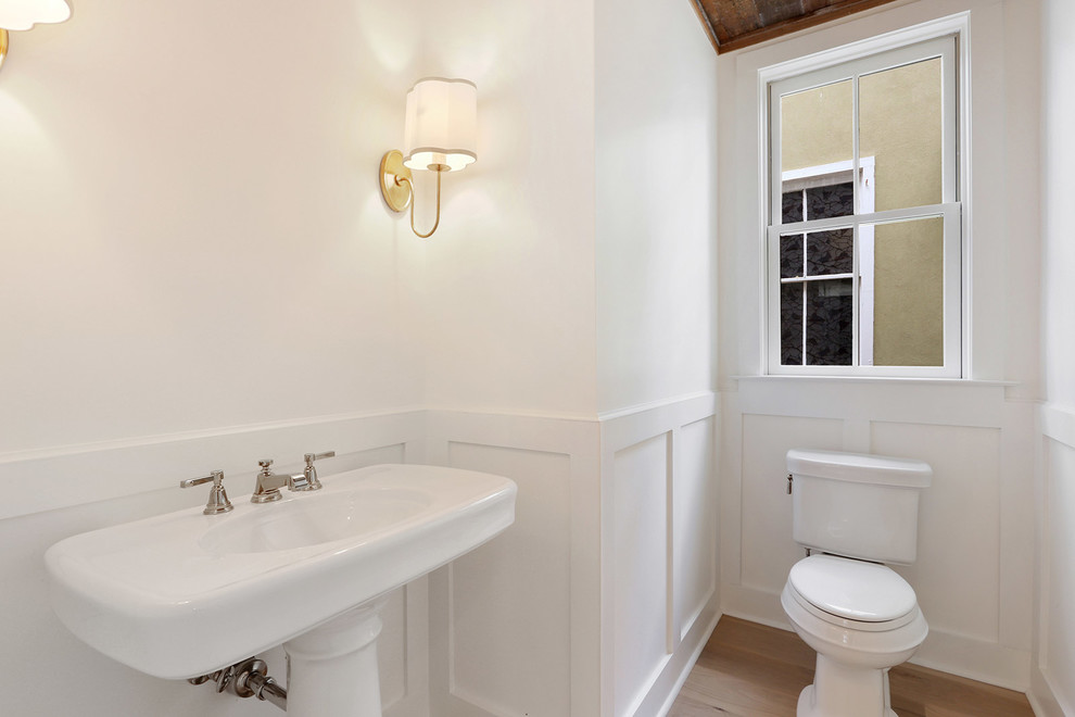 Mittelgroße Country Gästetoilette mit Wandtoilette mit Spülkasten, weißer Wandfarbe, hellem Holzboden und Sockelwaschbecken in Charleston