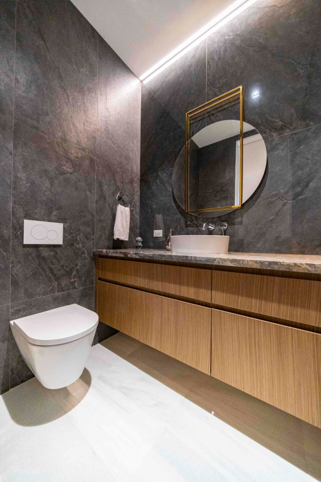 Aménagement d'un WC suspendu contemporain en bois brun de taille moyenne avec un placard en trompe-l'oeil, un carrelage gris, des carreaux de porcelaine, un mur gris, un sol en marbre, une vasque, un plan de toilette en marbre, un sol blanc et un plan de toilette gris.