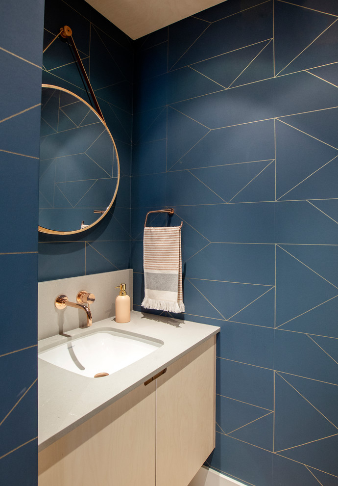 Bild på ett litet minimalistiskt grå grått toalett, med släta luckor, skåp i ljust trä, blå väggar, ljust trägolv, ett undermonterad handfat och bänkskiva i kvarts