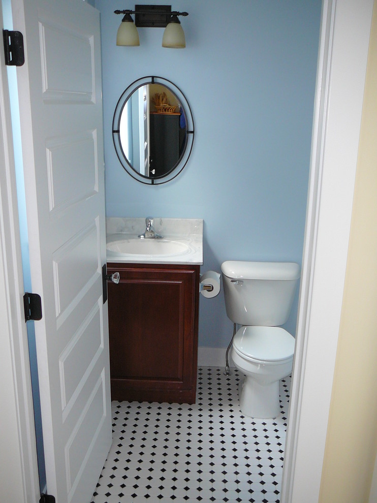 Aménagement d'un WC et toilettes craftsman en bois brun de taille moyenne avec un placard avec porte à panneau surélevé, WC à poser, un mur bleu, un sol en carrelage de porcelaine, un lavabo encastré et un plan de toilette en marbre.