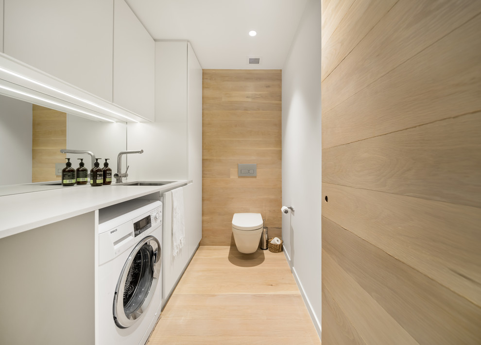 Idée de décoration pour un WC suspendu design avec un placard à porte plane, des portes de placard blanches, un mur blanc, parquet clair, un lavabo encastré, un sol beige et un plan de toilette blanc.