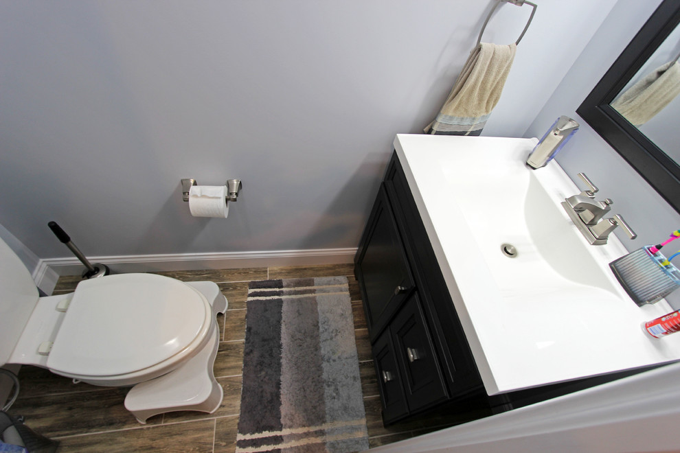 Cette photo montre un WC et toilettes chic de taille moyenne avec un placard à porte plane, des portes de placard grises, un mur gris, sol en stratifié et un sol marron.