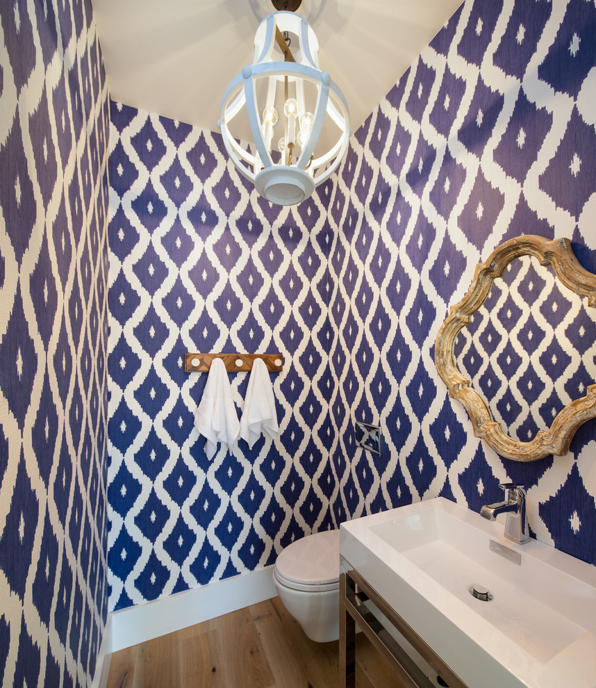 Inredning av ett eklektiskt litet toalett, med en vägghängd toalettstol, blå väggar, ljust trägolv, ett integrerad handfat, bänkskiva i akrylsten, öppna hyllor och brunt golv