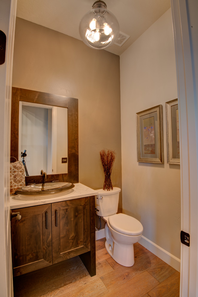 This is an example of a small traditional cloakroom in Boise with shaker cabinets, brown cabinets, a two-piece toilet, beige walls, light hardwood flooring, a vessel sink, solid surface worktops and brown floors.