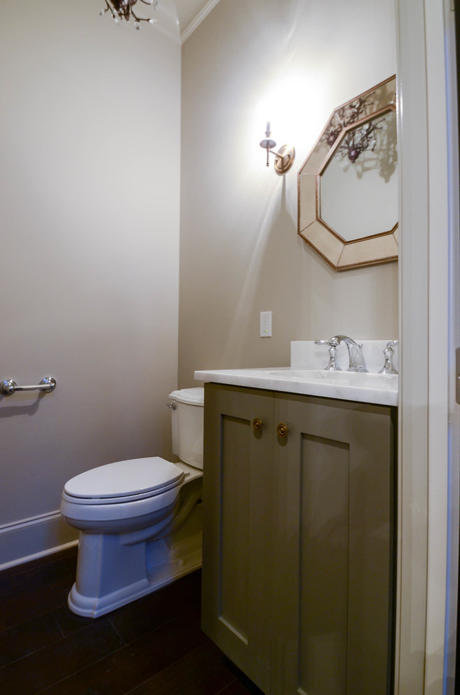 Cette photo montre un WC et toilettes chic de taille moyenne avec des portes de placard grises, parquet foncé, un lavabo encastré, un plan de toilette en marbre et un placard avec porte à panneau encastré.