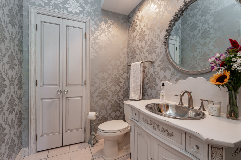 This is an example of a medium sized cloakroom in Other with freestanding cabinets, distressed cabinets, a two-piece toilet, blue walls, porcelain flooring, a built-in sink, wooden worktops, beige floors, white worktops, a freestanding vanity unit and wallpapered walls.