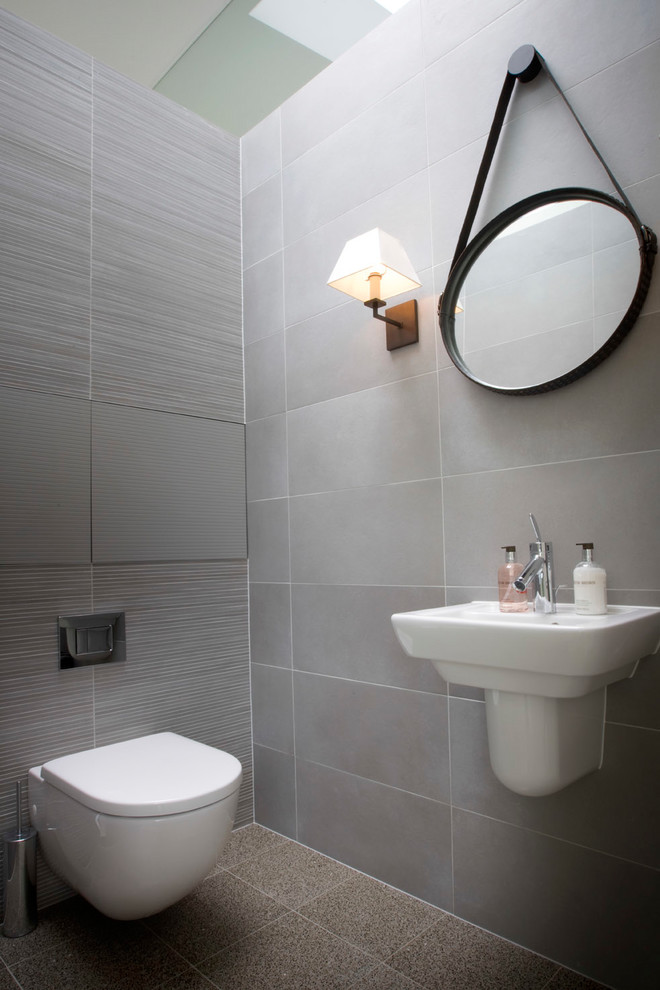 Immagine di un piccolo bagno di servizio design con WC sospeso, piastrelle grigie, piastrelle in ceramica, pareti grigie, pavimento in cemento e lavabo sospeso