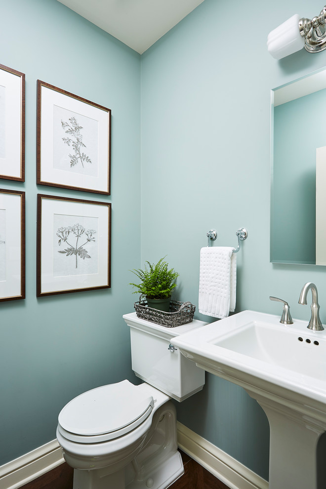 Diseño de aseo clásico con sanitario de dos piezas, paredes azules, suelo de madera oscura, lavabo con pedestal y suelo marrón