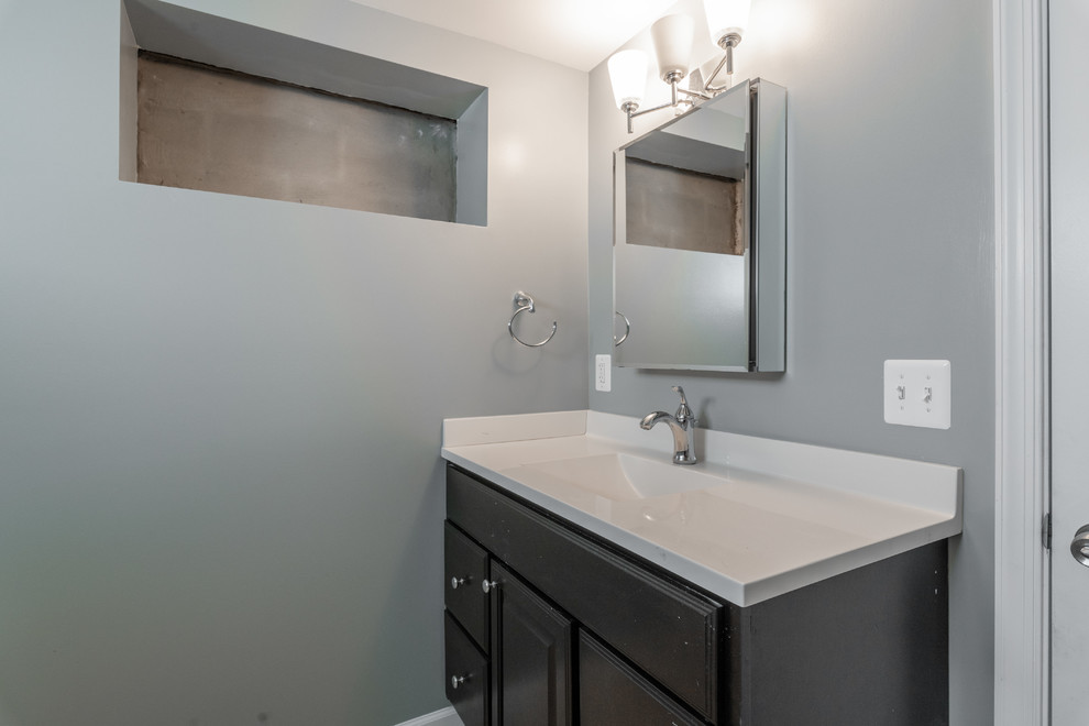Exemple d'un WC et toilettes tendance de taille moyenne avec un placard à porte shaker, des portes de placard grises, un mur gris, un lavabo intégré et un plan de toilette blanc.