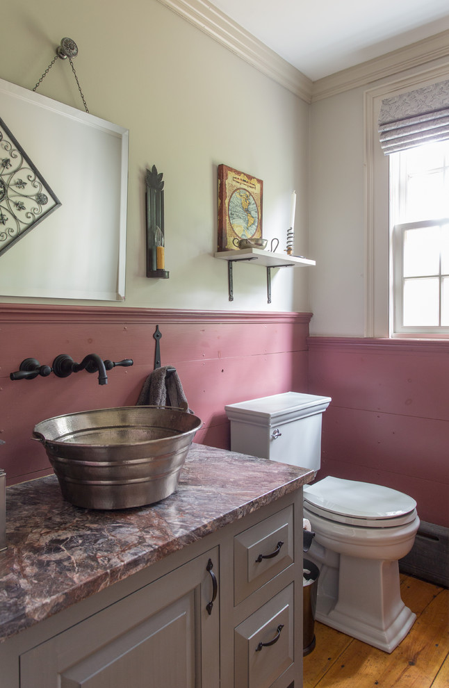 Kleine Country Gästetoilette mit Aufsatzwaschbecken, Marmor-Waschbecken/Waschtisch, grauen Schränken, rosa Wandfarbe, braunem Holzboden, Wandtoilette mit Spülkasten und profilierten Schrankfronten in Boston