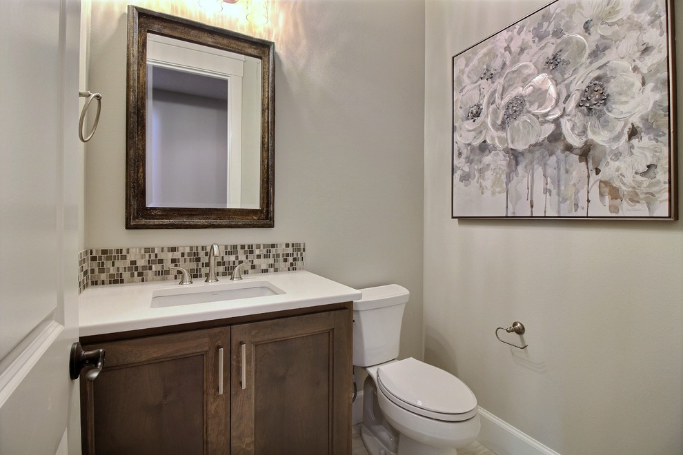 Réalisation d'un WC et toilettes craftsman en bois foncé de taille moyenne avec un placard avec porte à panneau encastré, WC séparés, un carrelage multicolore, des carreaux de céramique, un mur gris, un sol en carrelage de céramique, un lavabo encastré, un plan de toilette en quartz modifié, un sol gris et un plan de toilette blanc.