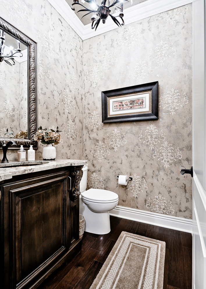 Example of a huge classic dark wood floor and brown floor powder room design in Other with raised-panel cabinets, medium tone wood cabinets, a one-piece toilet, an undermount sink, granite countertops and beige countertops
