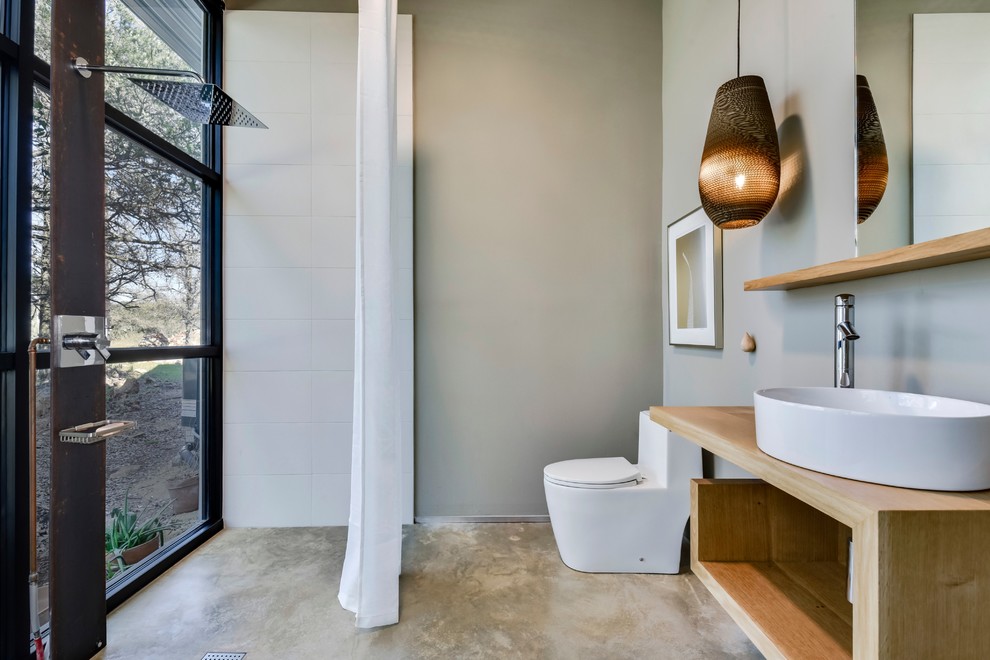 Inspiration for an industrial cloakroom in Austin with open cabinets, light wood cabinets, a one-piece toilet, white tiles, grey walls, concrete flooring, a vessel sink, wooden worktops, brown worktops and grey floors.