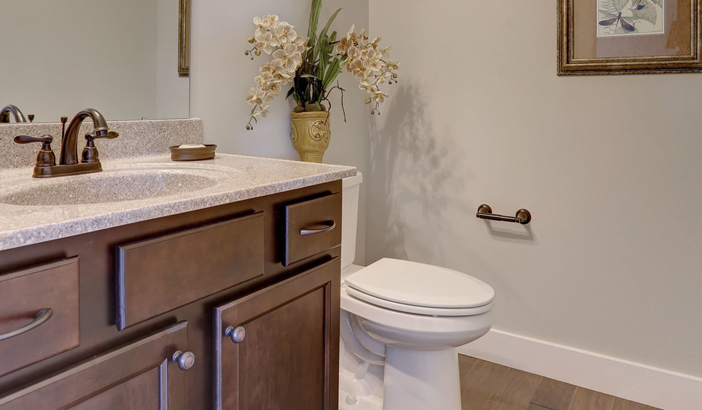Lantlig inredning av ett mellanstort beige beige toalett, med skåp i mellenmörkt trä, en toalettstol med separat cisternkåpa, beige väggar, mellanmörkt trägolv, ett integrerad handfat och bänkskiva i kvarts