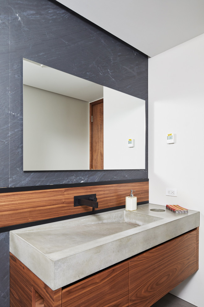Immagine di un bagno di servizio minimal con ante lisce, ante in legno scuro, pareti bianche, lavabo integrato, top in cemento e top grigio