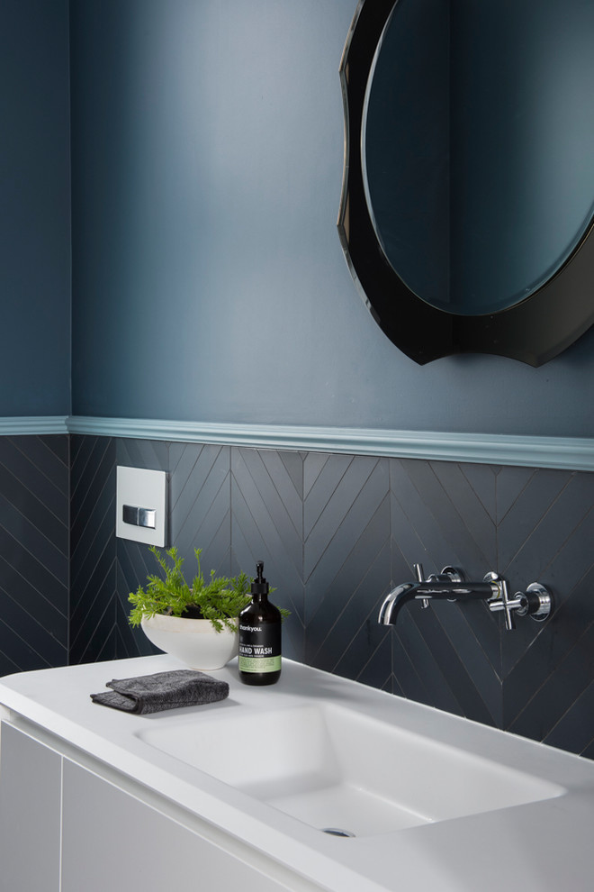 Inredning av ett modernt litet toalett, med möbel-liknande, vita skåp, en vägghängd toalettstol, blå kakel, keramikplattor, blå väggar, klinkergolv i keramik, ett integrerad handfat, bänkskiva i akrylsten och grått golv
