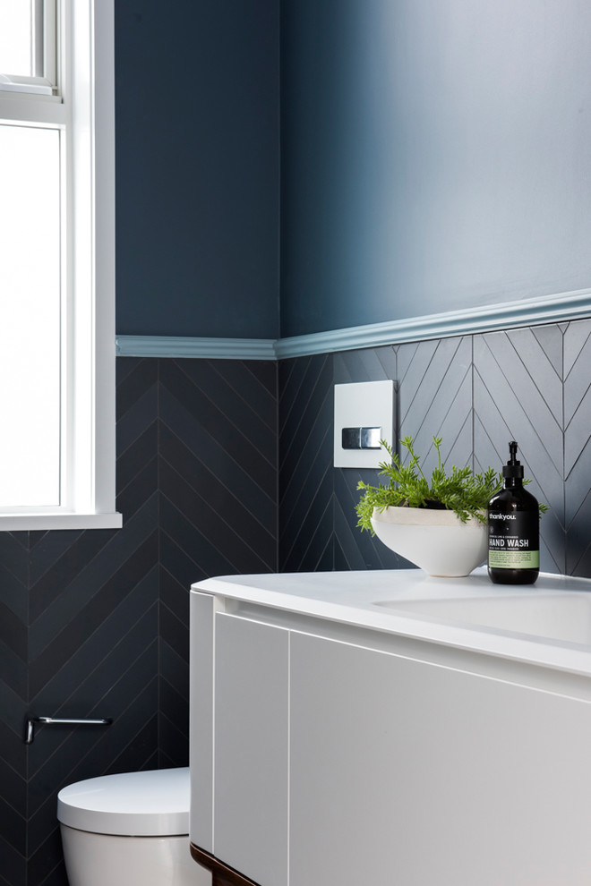 Inspiration pour un petit WC suspendu minimaliste avec un placard en trompe-l'oeil, des portes de placard blanches, un carrelage bleu, des carreaux de céramique, un mur bleu, un sol en carrelage de céramique, un lavabo intégré, un plan de toilette en surface solide et un sol gris.