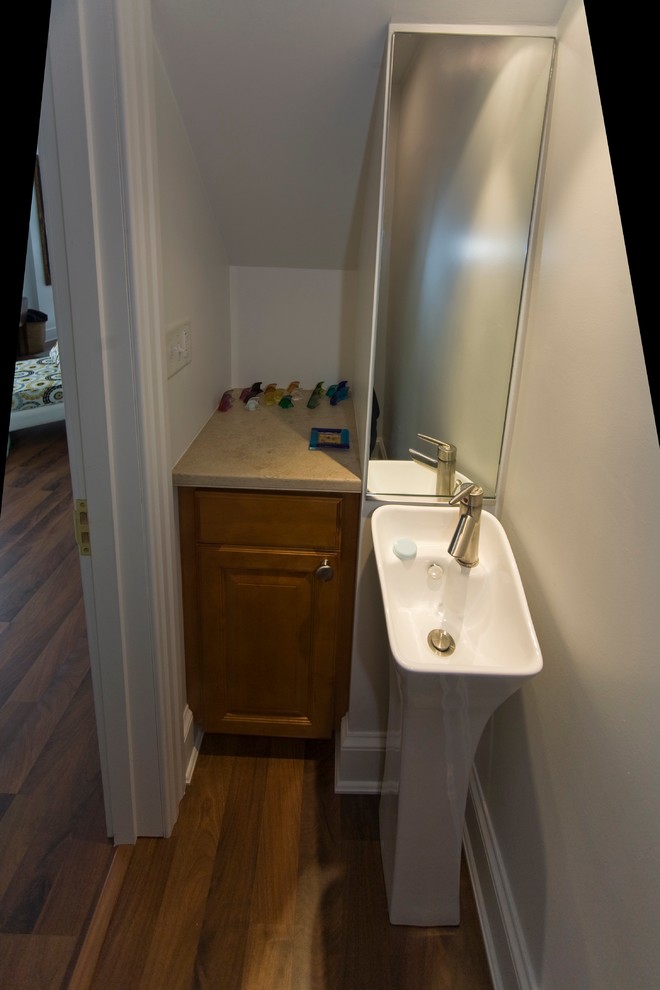 This is an example of a small contemporary cloakroom in Philadelphia with a pedestal sink, raised-panel cabinets, medium wood cabinets, solid surface worktops, a one-piece toilet, white walls and medium hardwood flooring.
