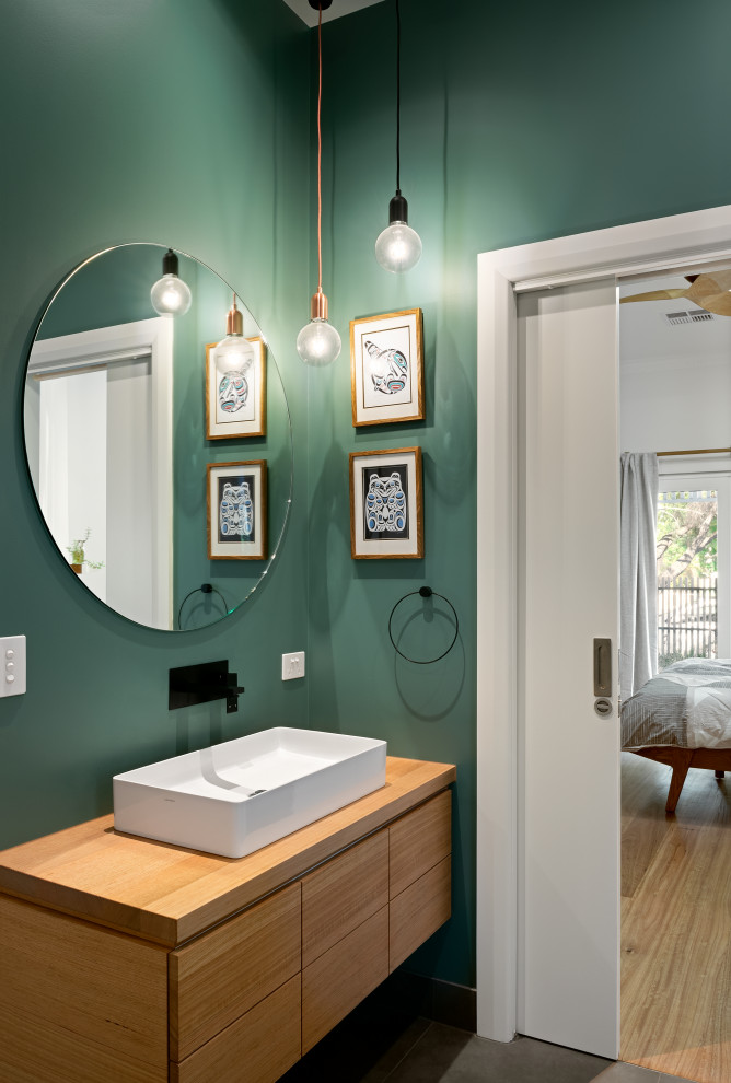 Moderne Gästetoilette mit flächenbündigen Schrankfronten, hellbraunen Holzschränken, grüner Wandfarbe, Aufsatzwaschbecken, Waschtisch aus Holz, grauem Boden, brauner Waschtischplatte und schwebendem Waschtisch in Melbourne