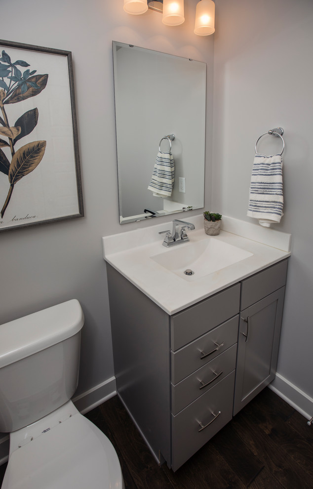 Exempel på ett amerikanskt toalett, med luckor med infälld panel, grå skåp, en toalettstol med hel cisternkåpa, grå väggar, mörkt trägolv, ett integrerad handfat, marmorbänkskiva och brunt golv