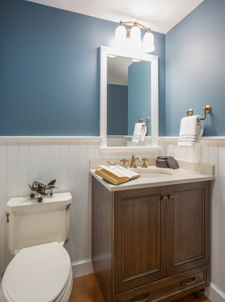 Inspiration for a timeless light wood floor powder room remodel in Boston with recessed-panel cabinets, medium tone wood cabinets, a one-piece toilet, blue walls, an undermount sink, quartz countertops and beige countertops