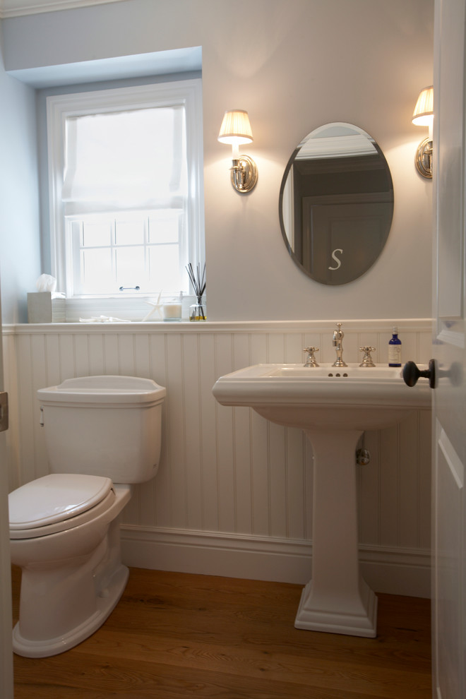 Ejemplo de aseo tradicional pequeño con lavabo con pedestal, sanitario de dos piezas, suelo de madera en tonos medios, paredes grises y puertas de armario blancas