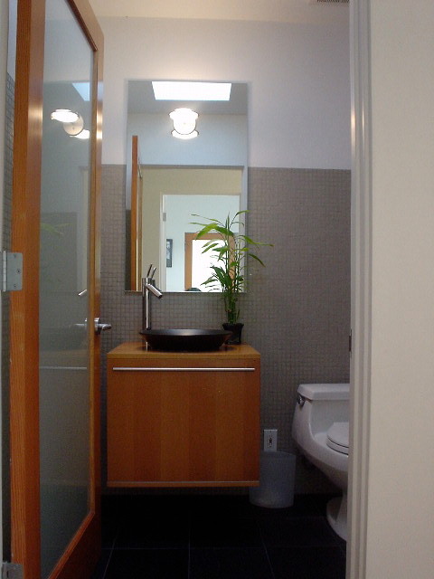 Immagine di un piccolo bagno di servizio minimalista con ante lisce, ante in legno chiaro, WC monopezzo, piastrelle grigie, piastrelle di vetro, pareti bianche, pavimento in ardesia, lavabo a bacinella, top in legno e pavimento nero