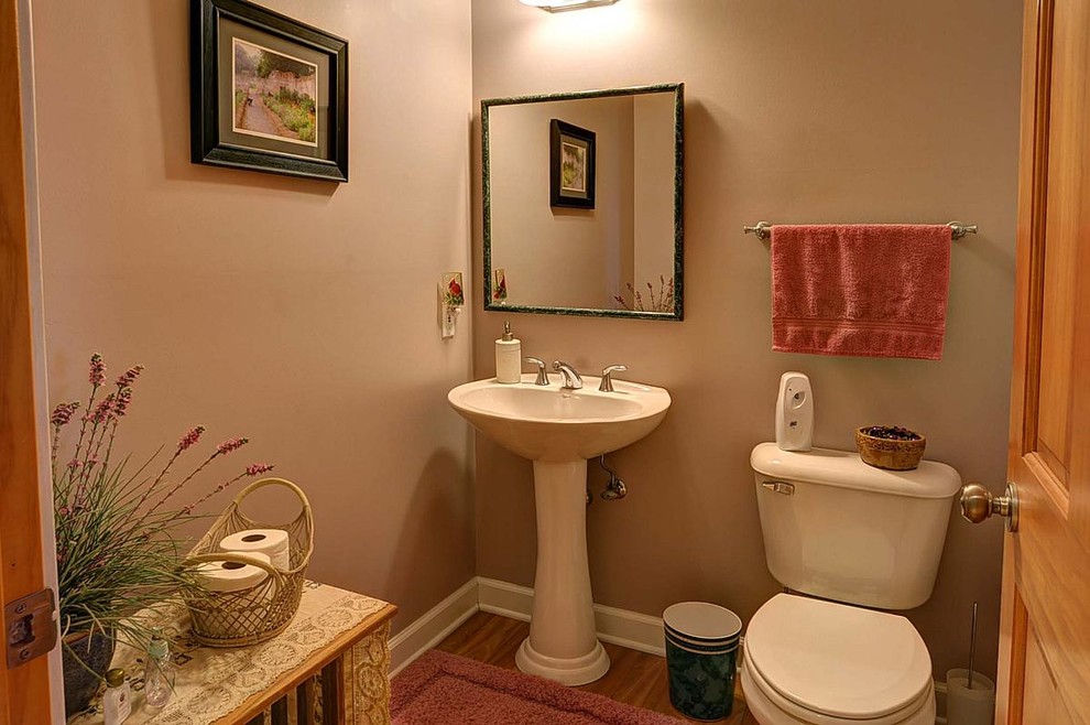 Mittelgroße Rustikale Gästetoilette mit hellbraunen Holzschränken, Wandtoilette mit Spülkasten, beiger Wandfarbe, Sockelwaschbecken und braunem Holzboden in Milwaukee