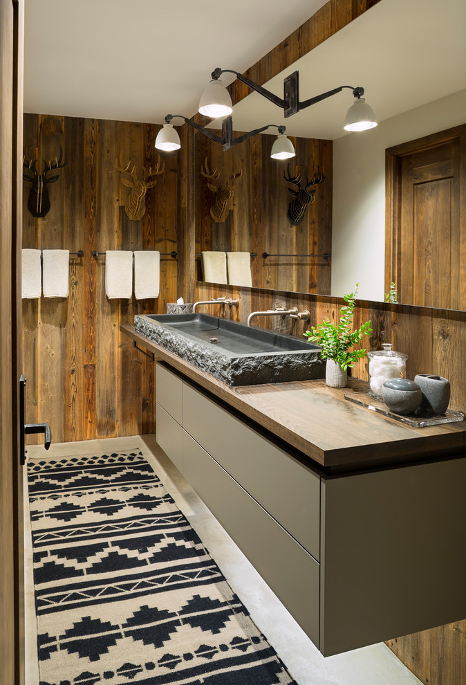 На фото: туалет в стиле рустика с плоскими фасадами, серыми фасадами, коричневыми стенами, бетонным полом, раковиной с несколькими смесителями, столешницей из дерева и коричневой столешницей с