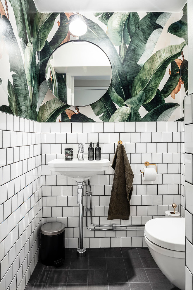 ヨーテボリにある小さな北欧スタイルのおしゃれなトイレ・洗面所 (オープンシェルフ、白いキャビネット、壁掛け式トイレ、白いタイル、セラミックタイル、白い壁、セラミックタイルの床、黒い床、黒い洗面カウンター、ペデスタルシンク) の写真