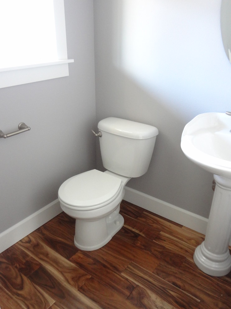 Ejemplo de aseo clásico pequeño con sanitario de dos piezas, paredes grises, suelo de madera en tonos medios y lavabo con pedestal