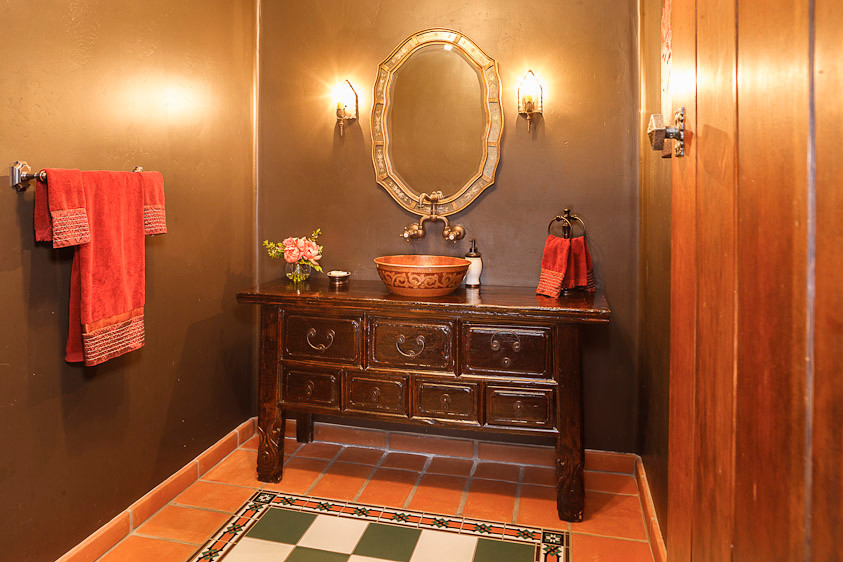 This is an example of a medium sized mediterranean cloakroom in San Diego with freestanding cabinets, dark wood cabinets, orange tiles, multi-coloured tiles, terracotta flooring, a vessel sink and wooden worktops.
