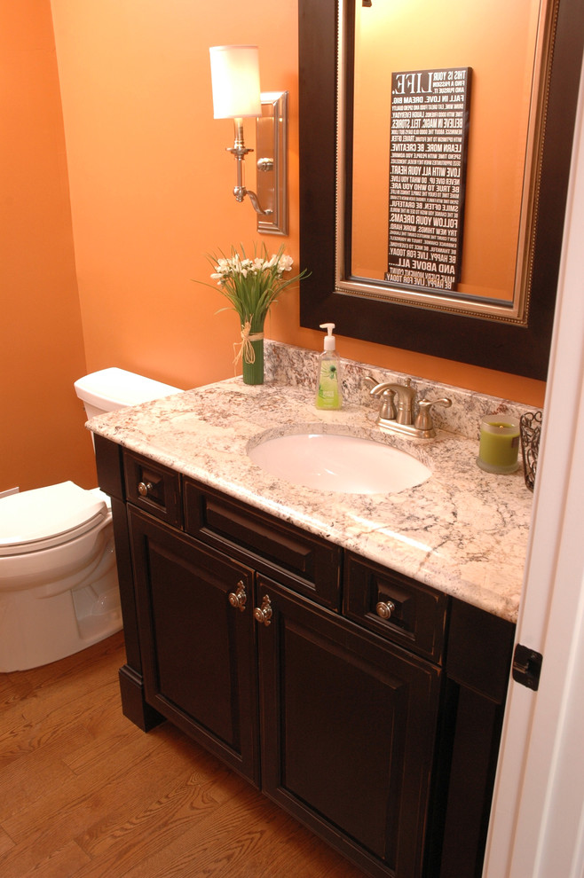 Ispirazione per un piccolo bagno di servizio classico con lavabo sottopiano, consolle stile comò, ante nere, top in granito, pareti arancioni e pavimento in legno massello medio
