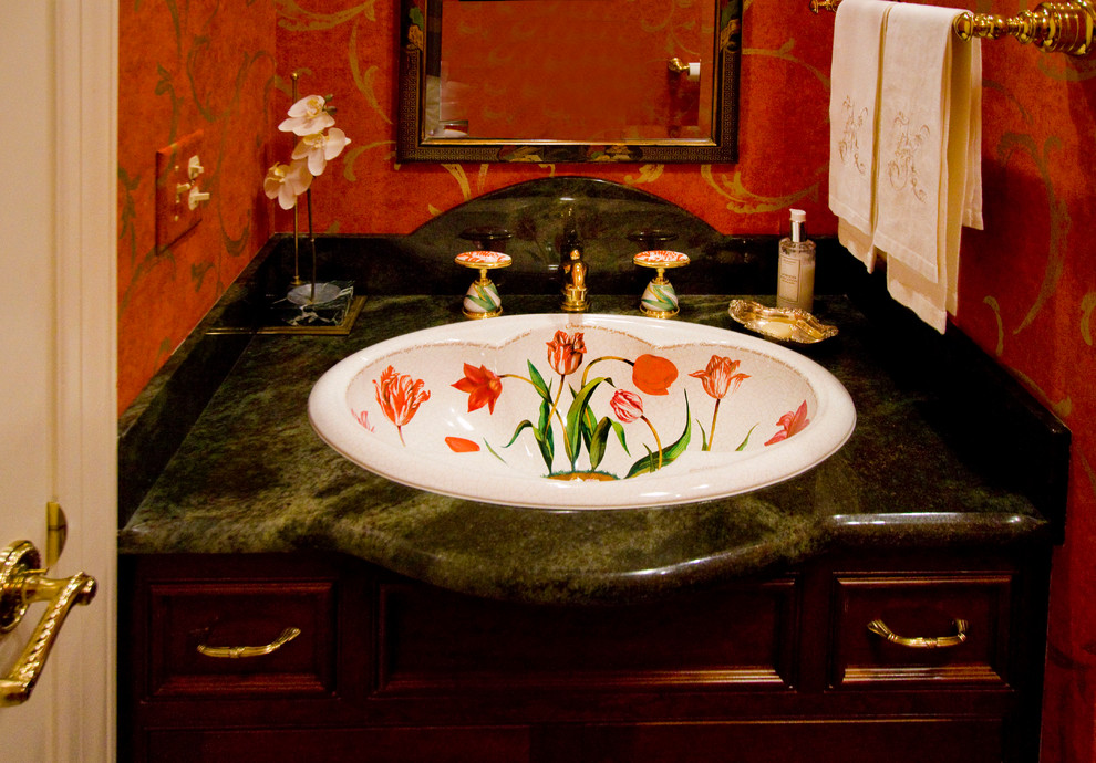 Klassisk inredning av ett litet toalett, med mellanmörkt trägolv, ett nedsänkt handfat, möbel-liknande, skåp i mörkt trä, granitbänkskiva och röda väggar