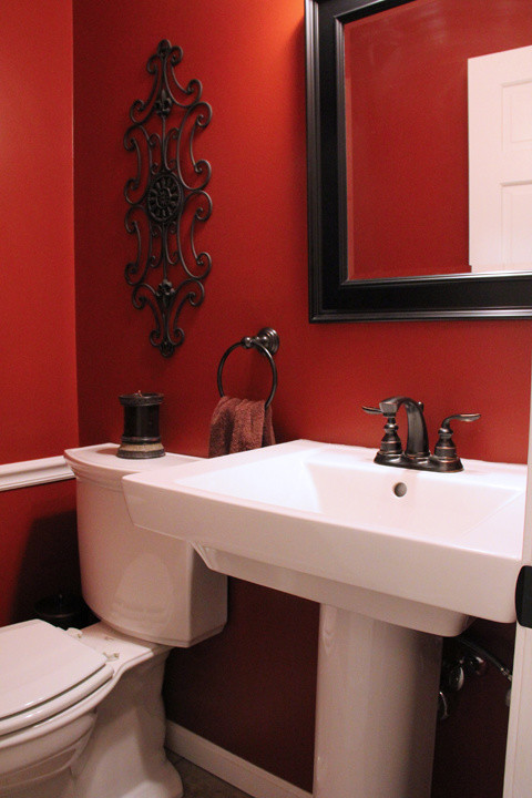 Modelo de aseo clásico pequeño con lavabo con pedestal, sanitario de dos piezas, paredes rojas y suelo de baldosas de porcelana