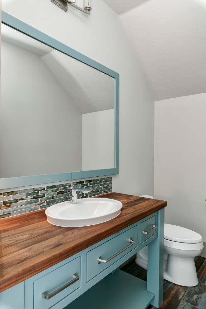 Exempel på ett mellanstort lantligt brun brunt toalett, med släta luckor, grå väggar, turkosa skåp, blå kakel, mosaik, målat trägolv, ett nedsänkt handfat, träbänkskiva och flerfärgat golv