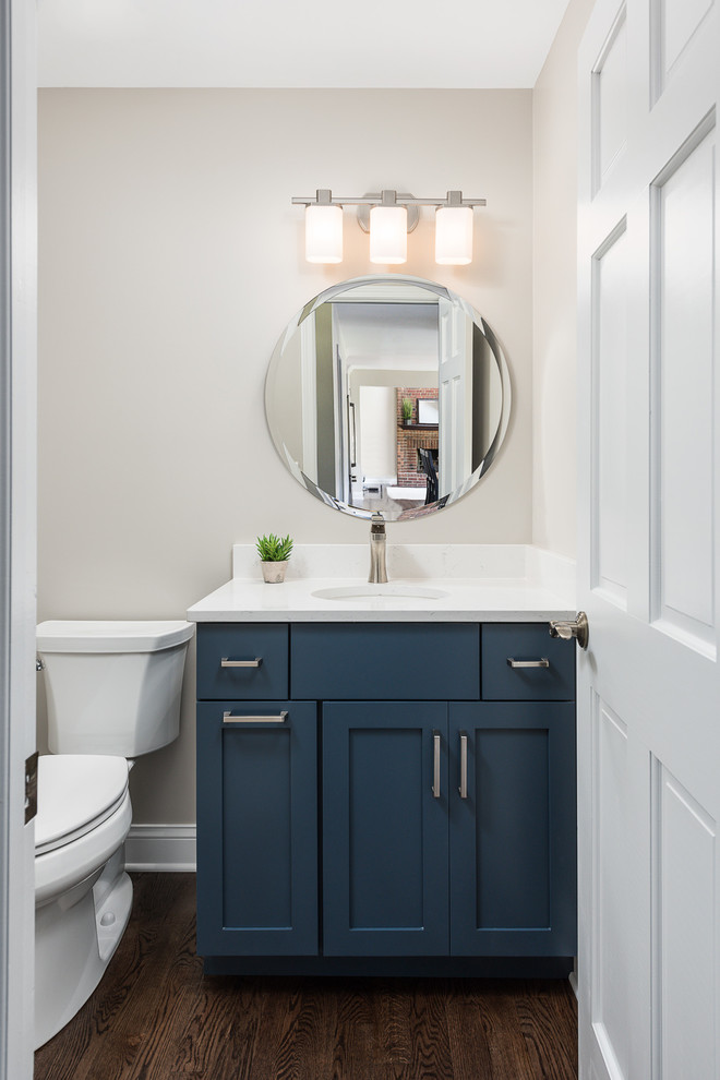 Klassisk inredning av ett litet vit vitt toalett, med luckor med infälld panel, blå skåp, en toalettstol med separat cisternkåpa, mellanmörkt trägolv, ett undermonterad handfat, bänkskiva i kvartsit, brunt golv och beige väggar