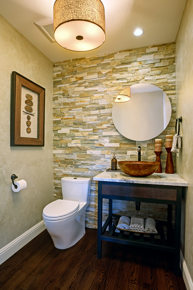 Inredning av ett modernt litet toalett, med ett fristående handfat, möbel-liknande, granitbänkskiva, en toalettstol med hel cisternkåpa, flerfärgad kakel, stenkakel, beige väggar och mörkt trägolv