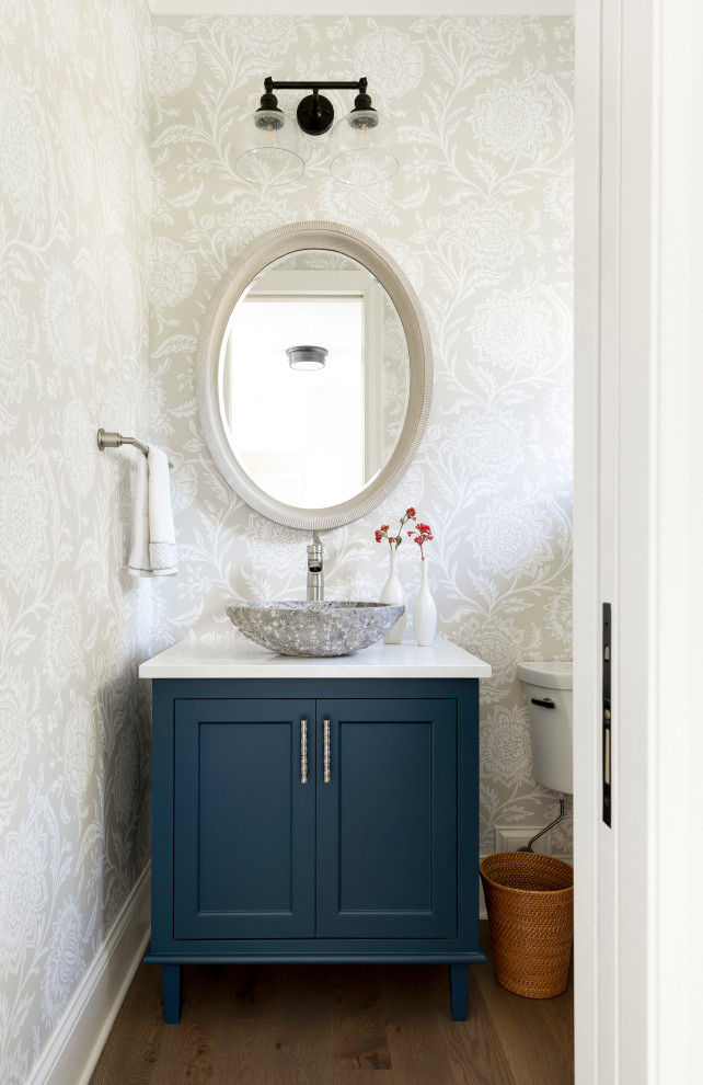 Powder room - mid-sized traditional medium tone wood floor and gray floor powder room idea in Minneapolis with recessed-panel cabinets, blue cabinets, a one-piece toilet, gray walls, a vessel sink, quartz countertops and white countertops