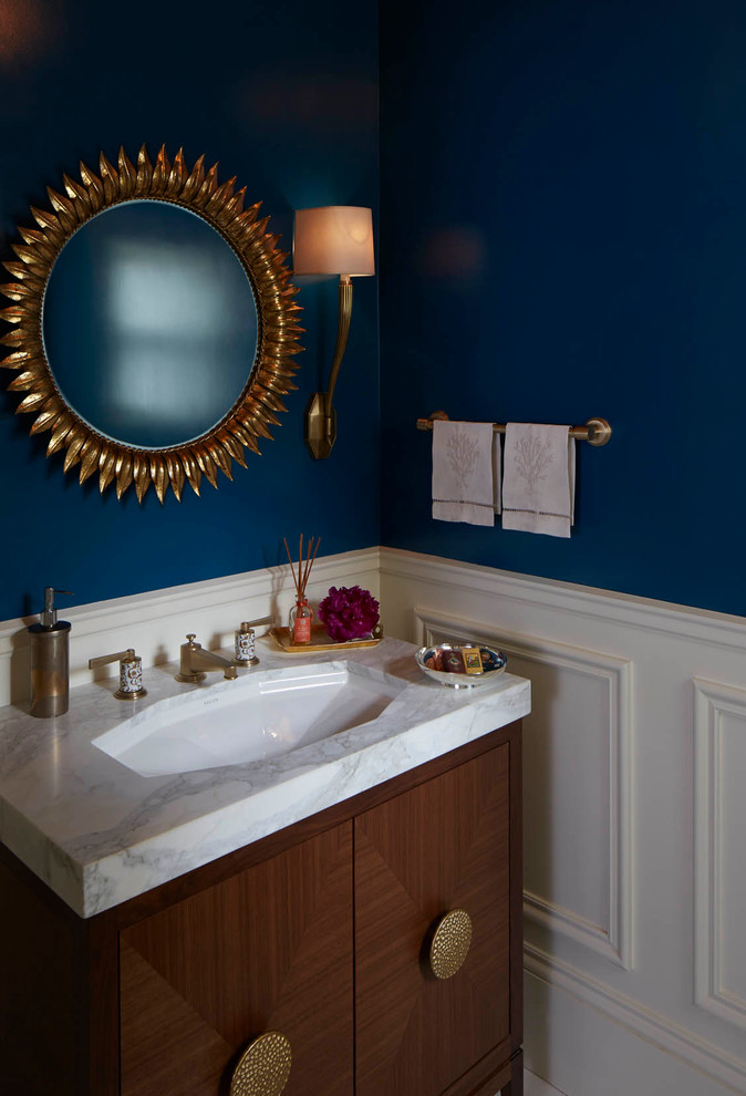 Diseño de aseo clásico renovado con lavabo bajoencimera, armarios tipo mueble, puertas de armario de madera oscura, encimera de mármol, paredes azules y encimeras blancas