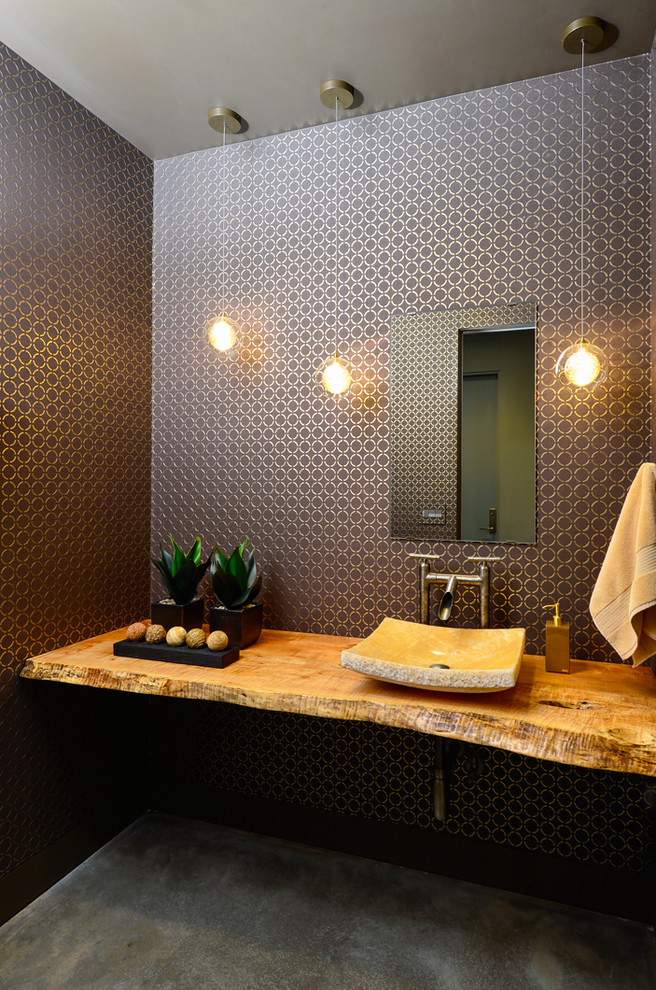 Powder room - mid-sized contemporary concrete floor powder room idea in Other with a vessel sink, wood countertops, multicolored walls and brown countertops